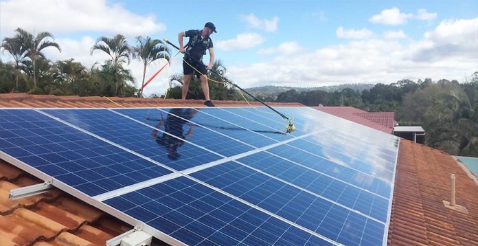 homem lavando painéis solares num telhado