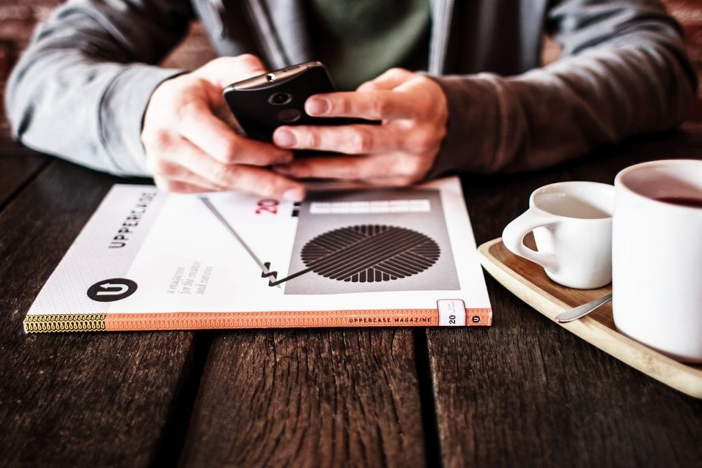 os 10 melhores livros de empreendedorismo - na foto homem usando o smartphone sentado a uma mesa com chávenas de café e um livro