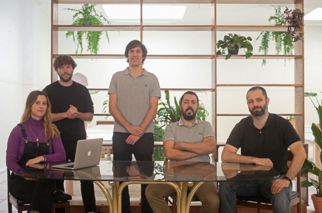 grupo de pessoas da equipa da BUK posando para a fotografia em volta de uma mesa, frente a uma estante com plantas.