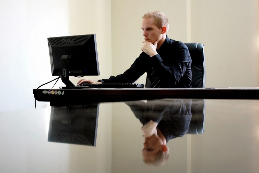 homem trabalhado num computador, com o seu reflexo espelhado no tampo da secretária