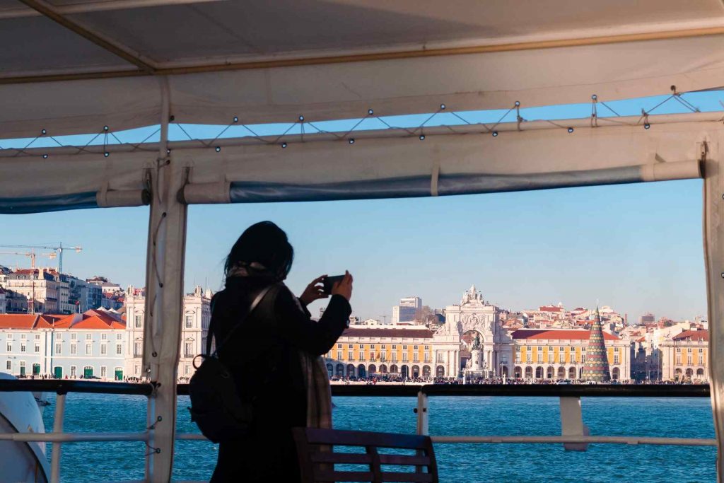 Mulher na coberta de um navio, fotografando a Baixa de Lisboa.