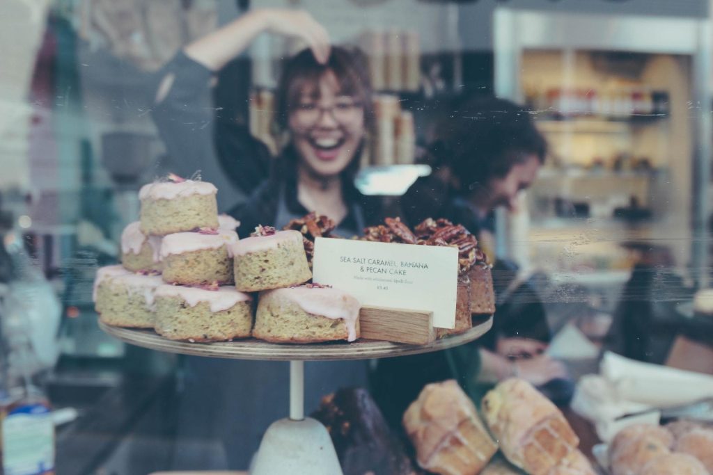 Mulher sorrindo dentro de uma montra de loja de bolos