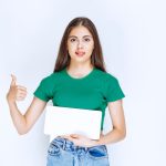 young-beautiful-woman-in-green-shirt-showing-blank-speech-frame-on-white-background